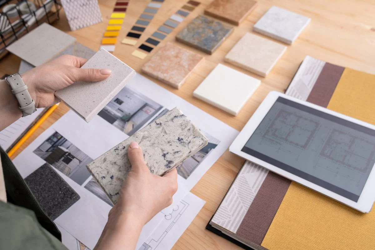 Designer comparing quartz and granite countertop samples over floor plans and material swatches by RnD Builders Inc