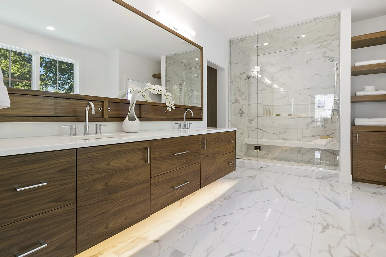 Luxury master bathroom with walnut floating vanity, dual sinks, and marble-tiled walk-in shower by RnD Builders Inc