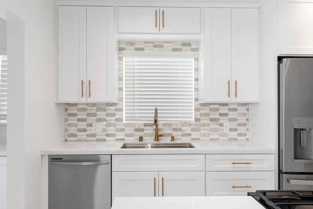 White shaker kitchen cabinets with brushed gold hardware and elongated hexagon tile backsplash by RnD Builders Inc
