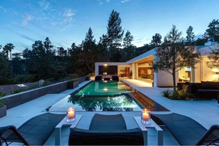 Luxury modern home with rectangular pool, candle lit lounge chairs, and open indoor-outdoor living at dusk by RnD Builders Inc