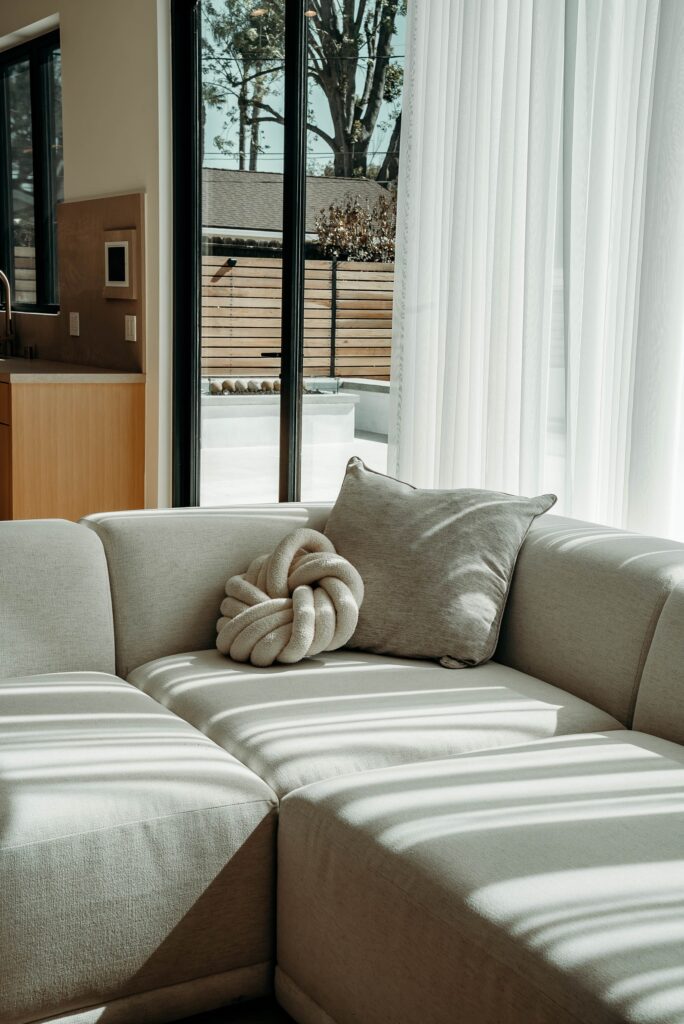 Modern open-concept living room with cream sectional sofa and floor-to-ceiling black-framed windows by RnD Builders Inc
