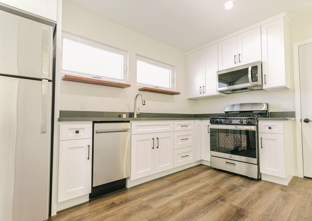 Inglewood ADU addition: White shaker cabinet kitchen with dark countertops, stainless steel appliances, and wood-look flooring in Inglewood by RnD Builders Inc