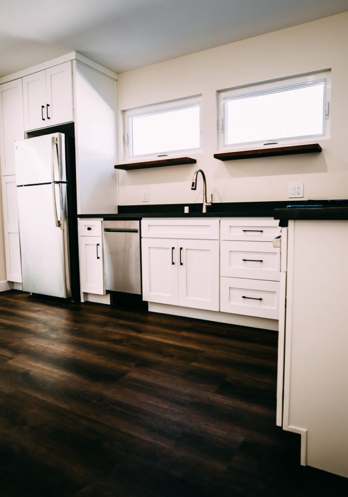 White Shaker Cabinet Kitchen with Dark Countertops Inglewood ADU addition: White shaker cabinet kitchen with dark countertops, floating wood shelves, and stainless appliances in Inglewood by RnD Builders Inc