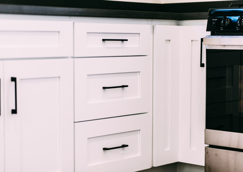 White Shaker-style Kitchen Base Cabinets White shaker-style kitchen base cabinets with black bar pulls and dark countertop by RnD Builders Inc
