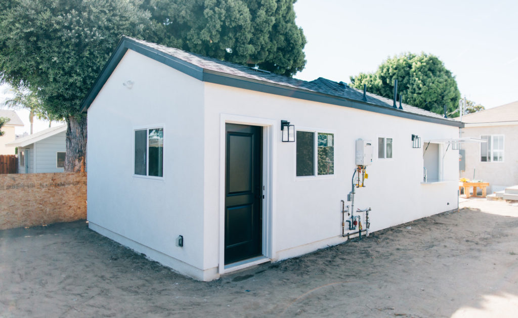 Hawthorne ADU & Addition Newly constructed white stucco ADU with dark entry door, gable roof, and solar panels by RnD Builders Inc