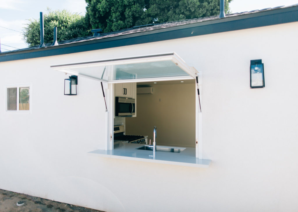 Modern ADU Exterior with Glass Bifold Pass-through Window Modern ADU exterior with glass bifold pass-through window, stainless sink, and open kitchen by RnD Builders Inc