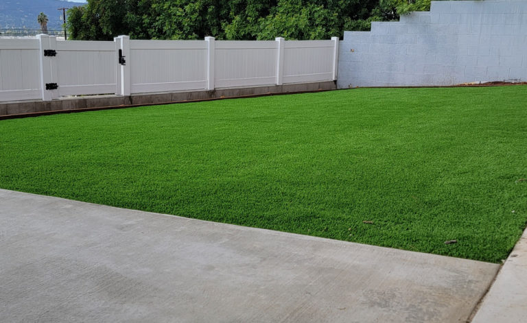 Backyard with artificial turf lawn, white vinyl privacy fence, and concrete pathway by RnD Builders Inc