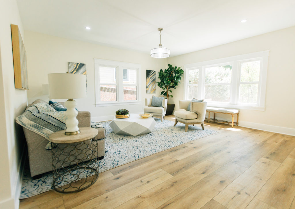 Bright living room with wide-plank hardwood floors, geometric coffee table, and cream accent chairs by RnD Builders Inc