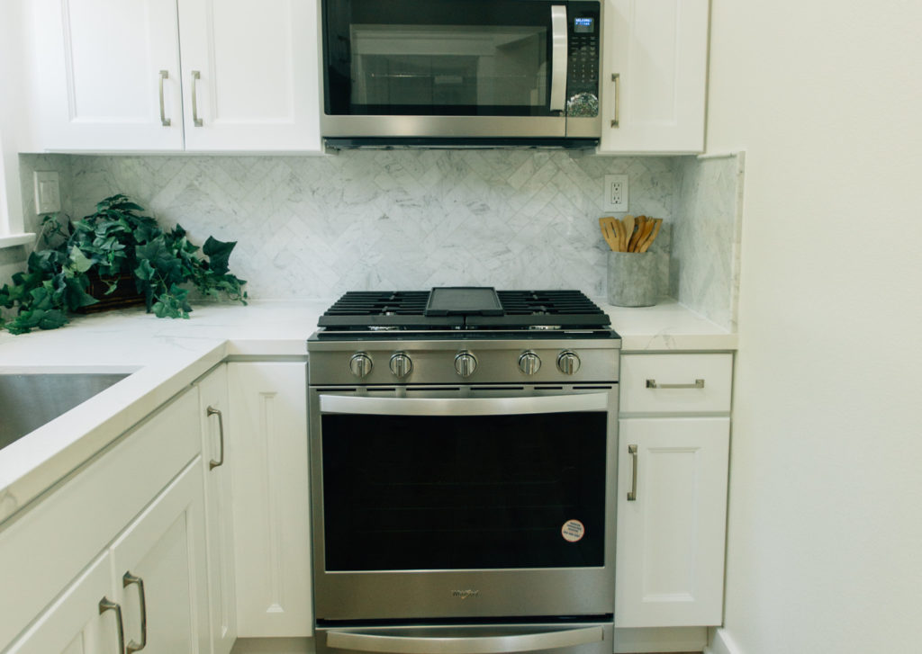Remodeling in Pasadena: White shaker kitchen with stainless steel Whirlpool gas range and marble herringbone backsplash by RnD Builders Inc