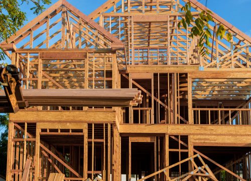 A wooden roof truss being lifted by a boom truck forklift in the roof of a new home
