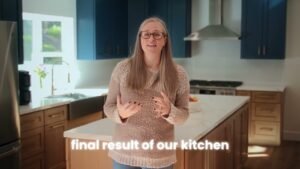 Woman standing in remodeled kitchen with navy cabinets, wood base cabinets, and marble island by RnD Builders Inc