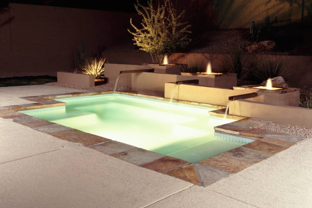 Illuminated Rectangular Pool with Raised Spa Illuminated rectangular pool with raised spa, sheet waterfalls, and desert landscaping at night by RnD Builders Inc