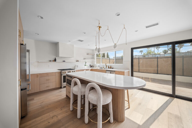 Open Kitchen with Oval Island and Sliding Door with light oak cabinetry, an oval island with round-back stools and a black-framed slider in Manhattan Beach by RnD Builders Inc