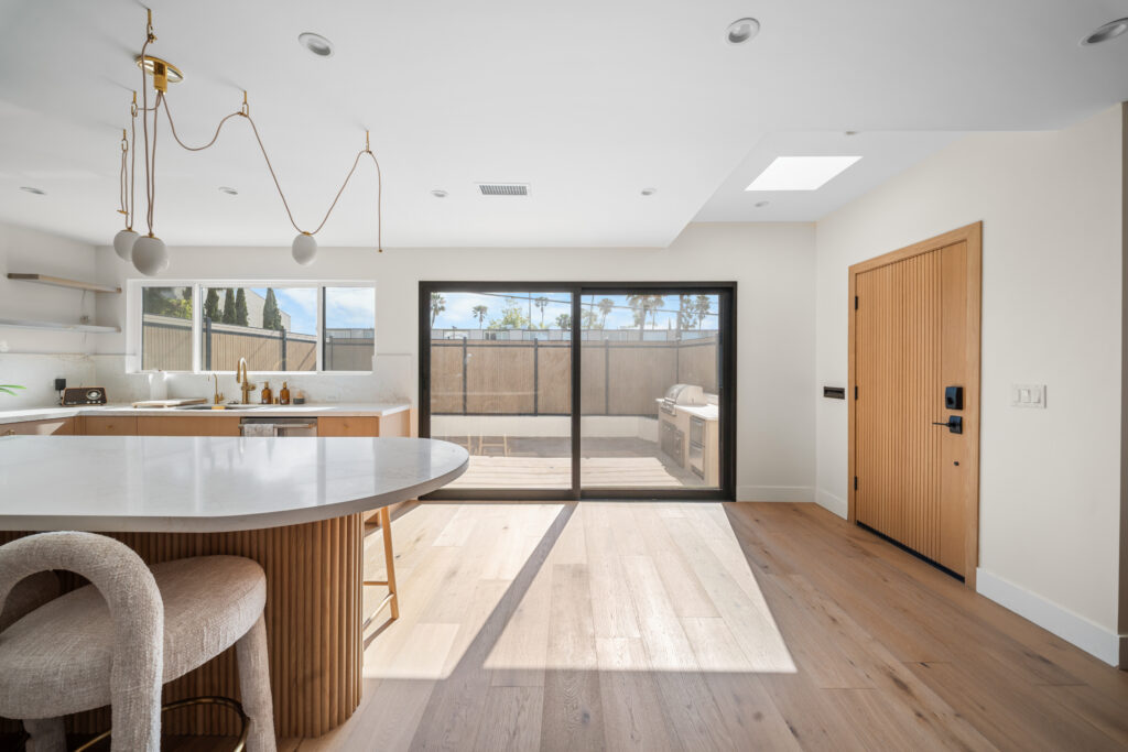 Kitchen and Dining Area Toward Front Door with an oval island, pendant lighting, wide-plank flooring and a wood front door in Manhattan Beach by RnD Builders Inc