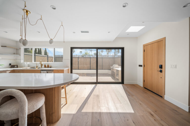 Kitchen and Dining Area Toward Front Door with an oval island, pendant lighting, wide-plank flooring and a wood front door in Manhattan Beach by RnD Builders Inc
