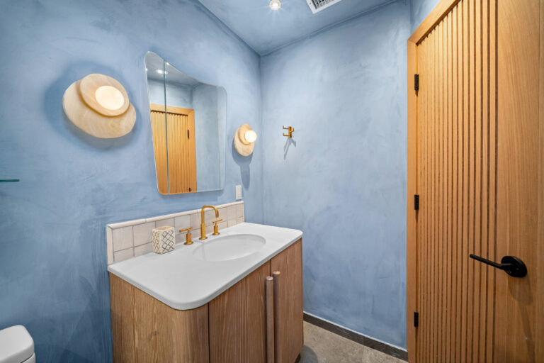 Blue Bathroom Vanity with Round Sconce with a wood vanity, a white sink, a round sconce and blue plaster walls in Manhattan Beach by RnD Builders Inc