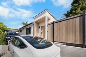manhattan-beach-home-remodel-by-rndbuildersinc-image-54 Modern exterior home with vertical wood slat gate, stucco facade, and concrete driveway by RnD Builders Inc
