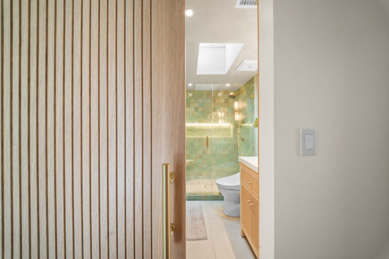 Fluted Wood Door Opening to Green Tile Bathroom with a fluted wood door and a green tile shower beyond in Manhattan Beach by RnD Builders Inc