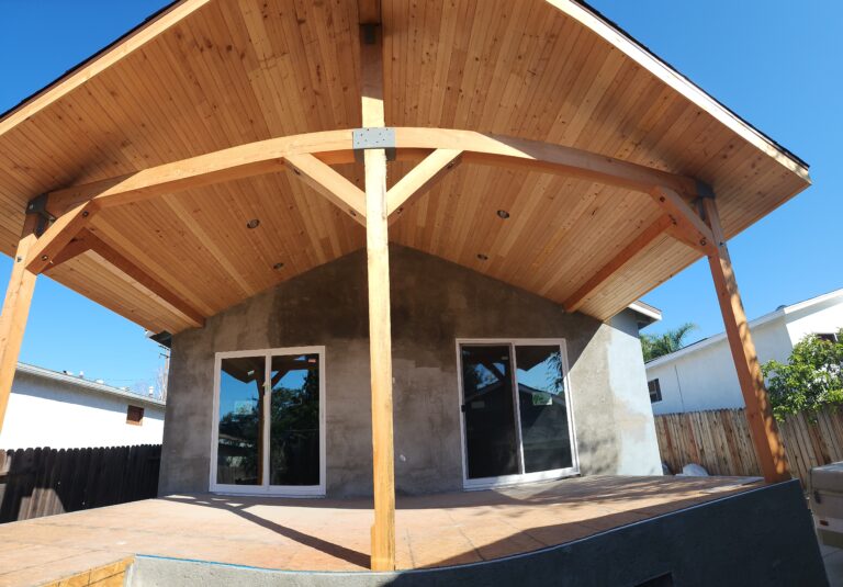 Vaulted wood-ceiling patio cover with heavy timber posts and sliding glass doors on stucco exterior by RnD Builders Inc