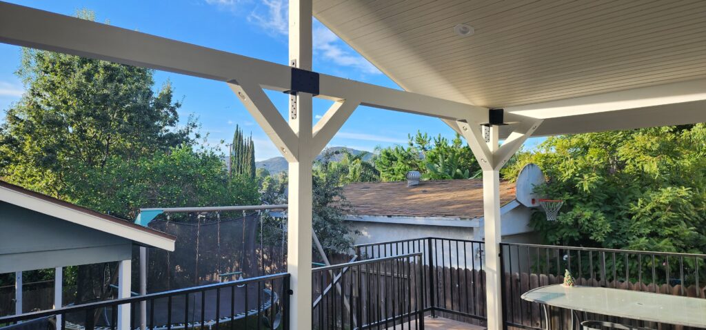 White painted wood patio cover with gabled roof and black metal railing on elevated deck by RnD Builders Inc