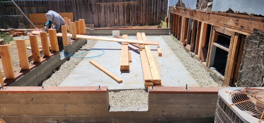 Residential addition foundation framing with concrete slab, gravel base, and lumber by RnD Builders Inc