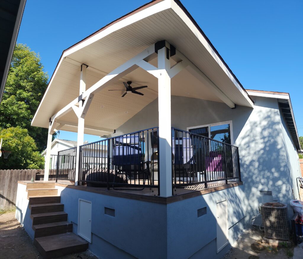 Covered elevated deck with gable roof, white timber frame, and black metal railing by RnD Builders Inc