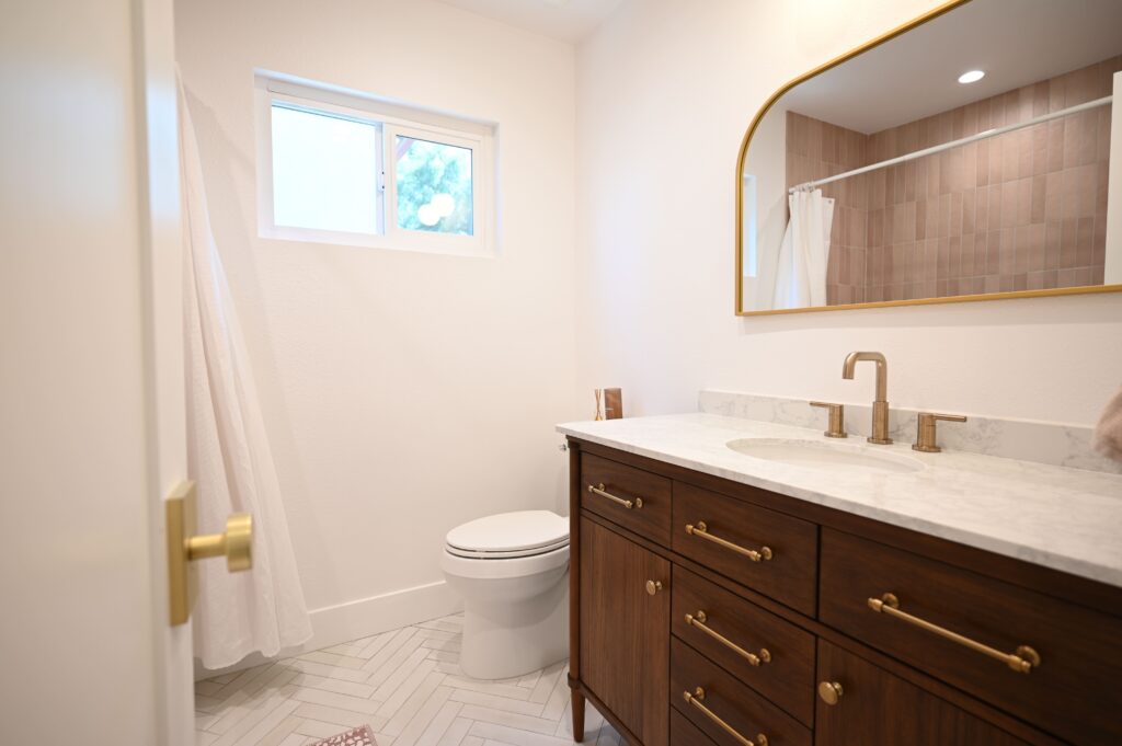 Remodeled bathroom with dark walnut vanity, marble countertop, herringbone tile floor, and brass fixtures by RnD Builders Inc