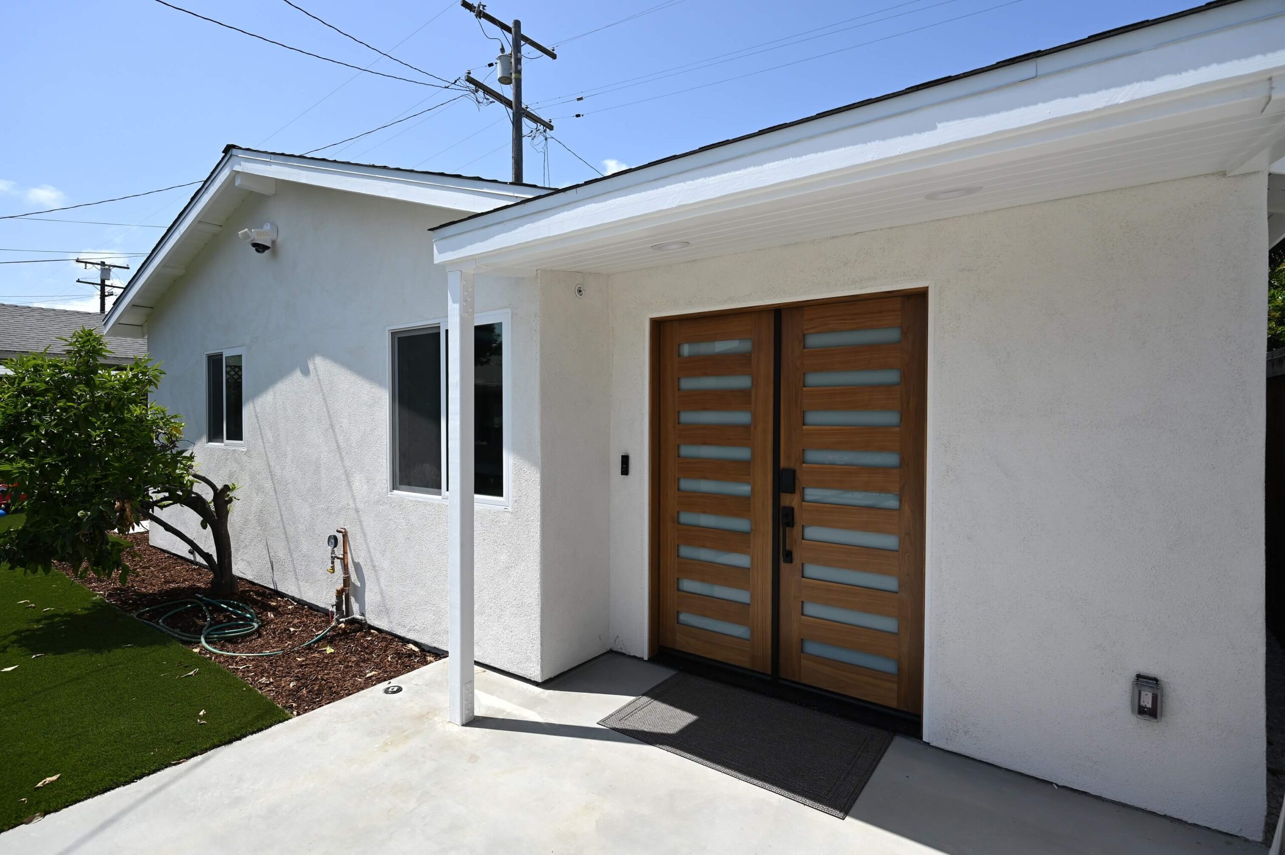 Modern ADU Exterior with Wood Double Entry Doors Modern ADU exterior with wood double entry doors and white stucco facade by RnD Builders Inc