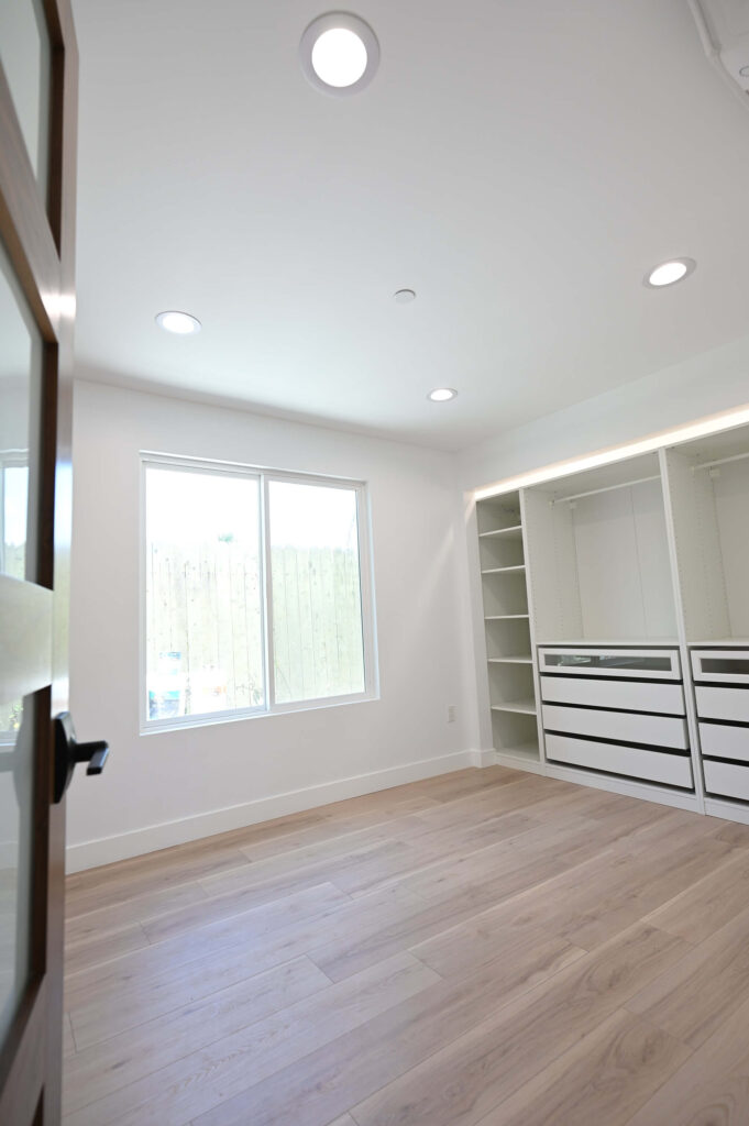 Bright Walk-in Closet with White Built-in Shelving Bright walk-in closet with white built-in shelving, drawers, and light wood flooring by RnD Builders Inc