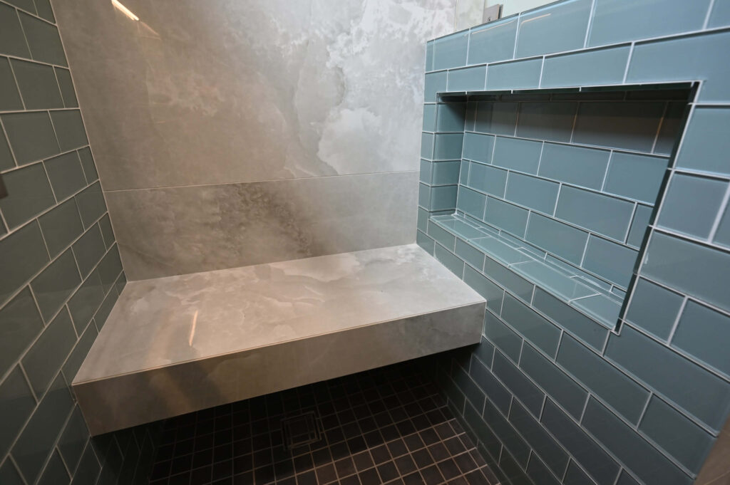 Walk-in Shower with Blue Glass Subway Tile Hawthorne 750 sqft ADU: Hawthorne 750 sqft ADU: Walk-in shower with blue glass subway tile, built-in niche, bench, and dark mosaic floor in Hawthorne by RnD Builders Inc