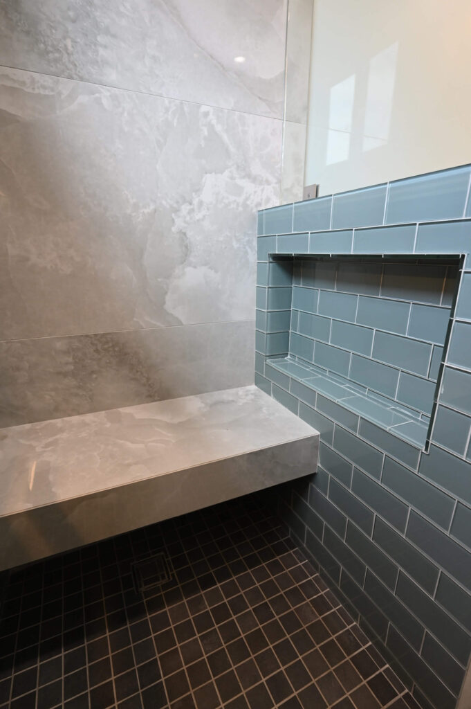 Walk-in Shower with Marble-look Porcelain Walls Hawthorne 750 sqft ADU: Hawthorne 750 sqft ADU: Walk-in shower with marble-look porcelain walls, blue glass subway tile niche, and floating bench in Hawthorne by RnD Builders Inc