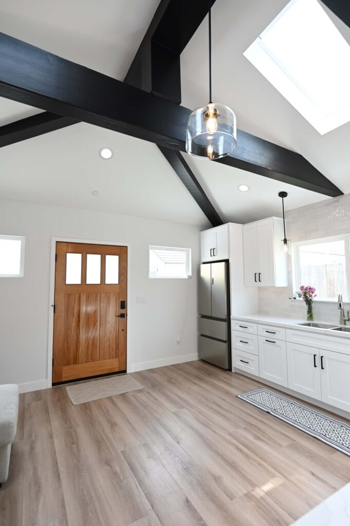 Open-plan ADU Interior with Vaulted Ceiling Open-plan ADU interior with vaulted ceiling, black exposed beams, skylight, and white shaker kitchen by RnD Builders Inc