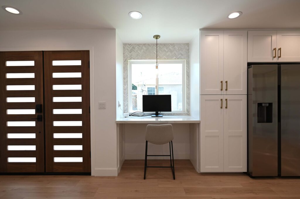Built-in Kitchen Desk Nook with Herringbone Tile Backsplash Built-in kitchen desk nook with herringbone tile backsplash, white shaker cabinets, and modern wood double entry door by RnD Builders Inc