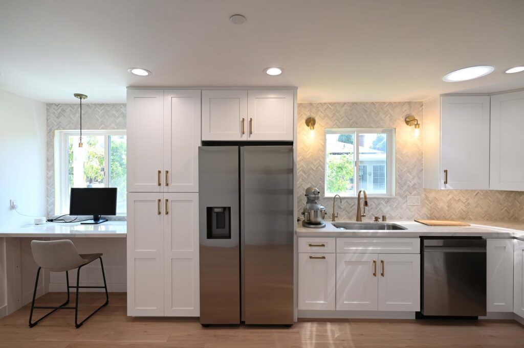 White Shaker Cabinet Kitchen Hawthorne 650 sqft ADU: Hawthorne 650 sqft ADU: White shaker cabinet kitchen with herringbone tile backsplash, stainless refrigerator, and built-in desk nook in Hawthorne by RnD Builders Inc