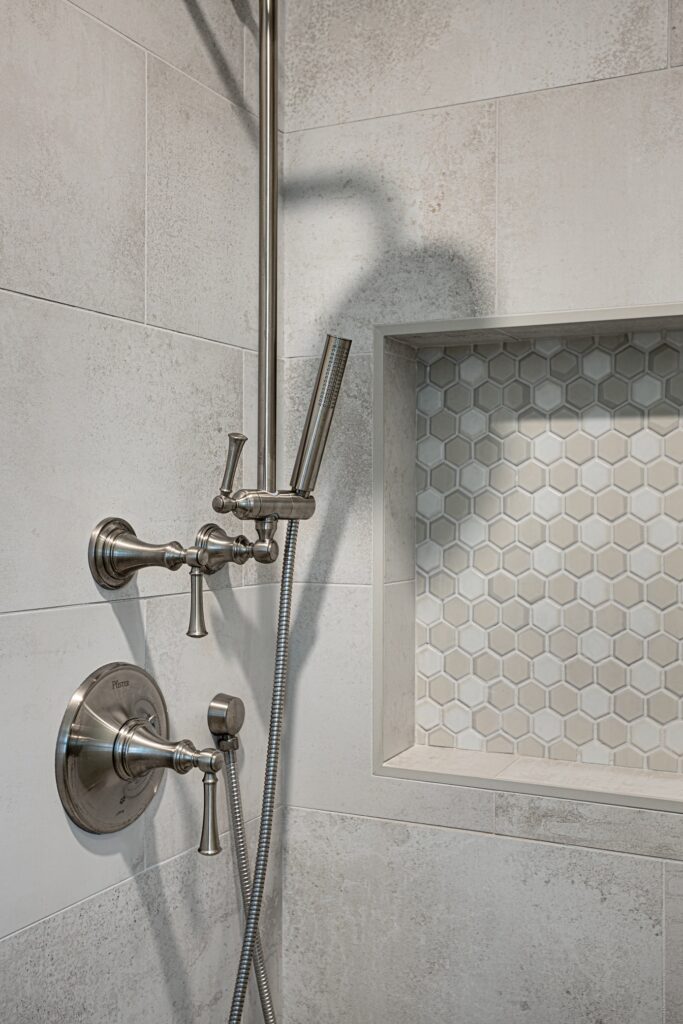 Thousand Oaks bathrooms remodel: Shower wall with brushed nickel Pfister fixtures, slide bar, handheld wand, and recessed hexagon tile niche in Thousand Oaks by RnD Builders Inc