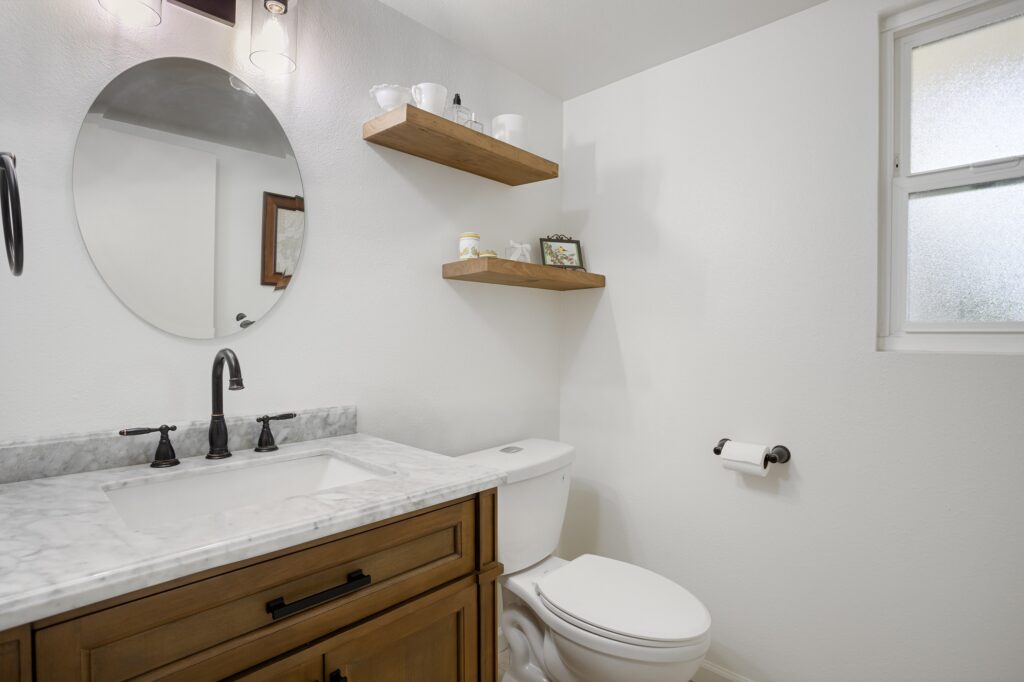 Thousand Oaks bathrooms remodel: Bathroom with wood vanity, marble countertop, round mirror, and floating shelves in Thousand Oaks by RnD Builders Inc