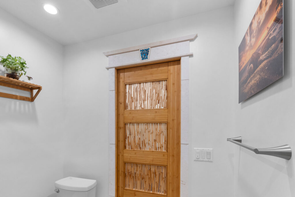 Bathroom with bamboo panel door, stone surround, blue mosaic accent, and wall-mounted toilet by RnD Builders Inc
