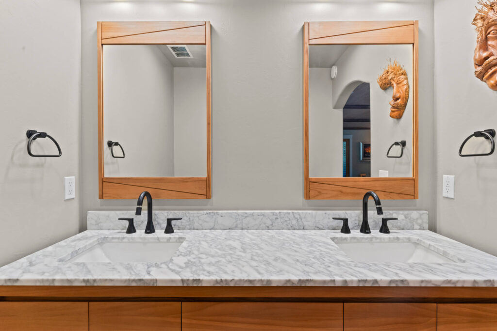 Thousand Oaks walnut bathroom: Double vanity bathroom with marble countertop, wood-framed mirrors, and matte black faucets in Thousand Oaks by RnD Builders Inc