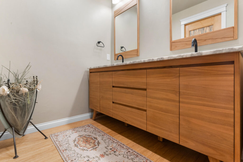 Thousand Oaks walnut bathroom: Mid-century modern bathroom vanity with warm wood cabinetry, marble countertop, and dual matte black faucets in Thousand Oaks by RnD Builders Inc