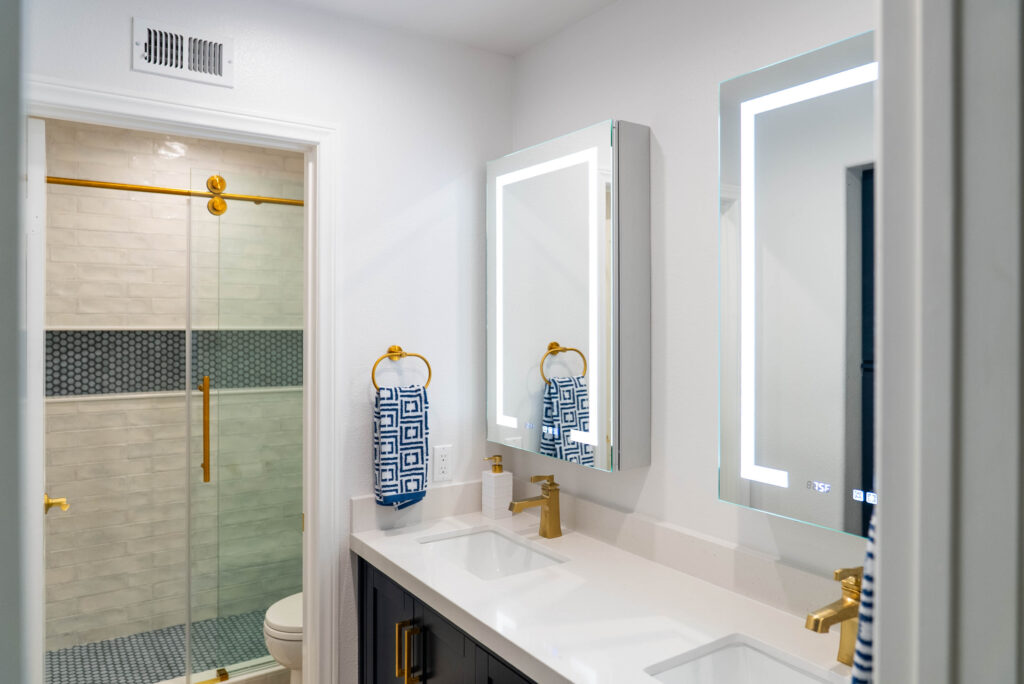 Modern bathroom with dual LED mirrors, gold fixtures, and tiled glass shower enclosure by RnD Builders Inc