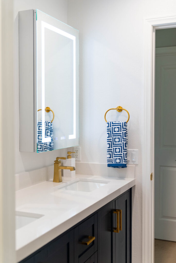 Oxnard bathroom remodel: Bathroom vanity with navy shaker cabinets, white quartz countertop, gold faucet, and LED mirror in Oxnard by RnD Builders Inc