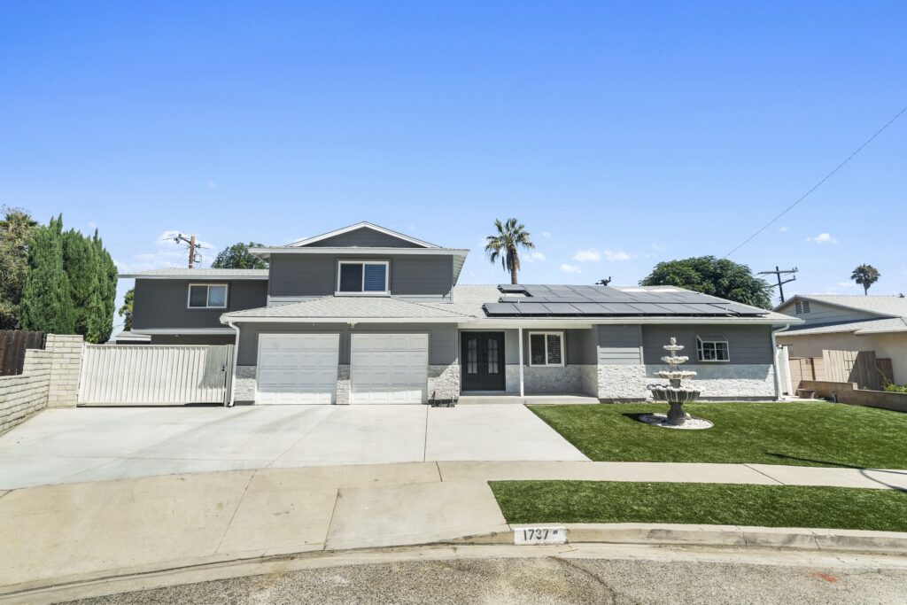 Simi Valley exterior remodel: Two-story gray exterior home remodel with solar panels, three-car garage, and artificial turf front yard in Simi Valley by RnD Builders Inc