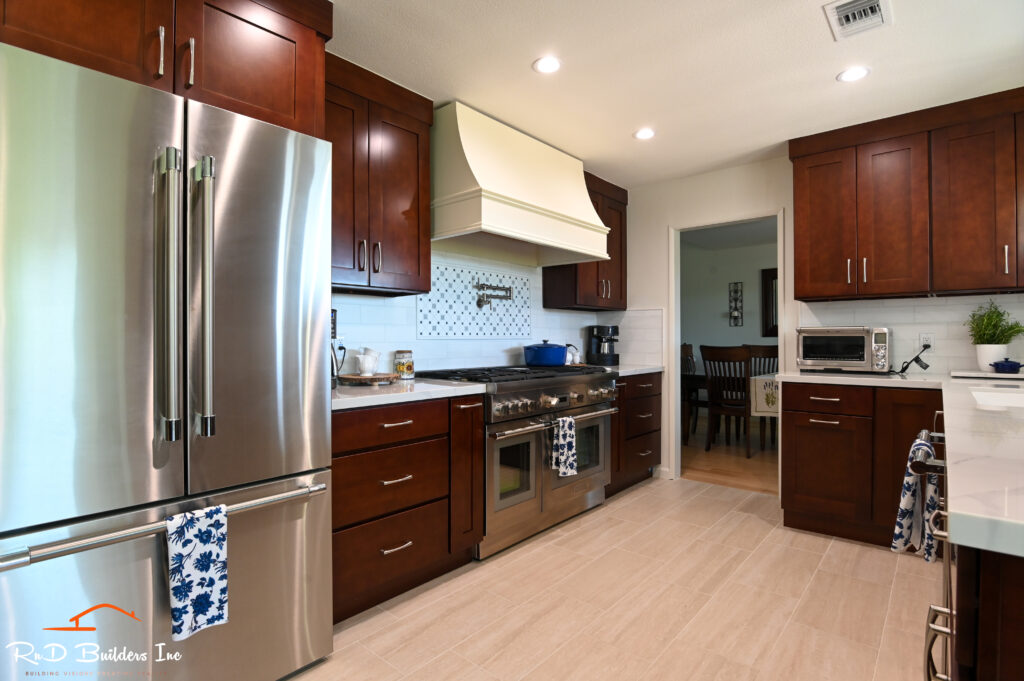 Traditional Kitchen with Dark Cherry Shaker Cabinets in Westlake Village Traditional kitchen with dark cherry shaker cabinets, stainless appliances, and cream decorative range hood in Westlake Village by RnD Builders Inc