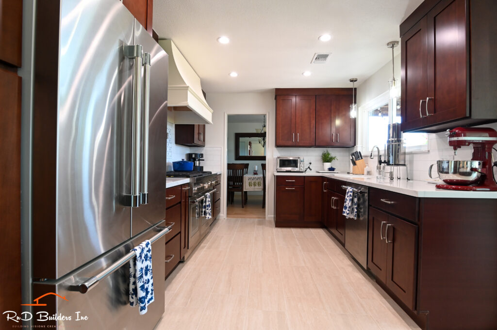 Westlake Village cherry kitchen: Galley kitchen with dark cherry shaker cabinets, stainless steel appliances, and light tile flooring in Westlake Village by RnD Builders Inc