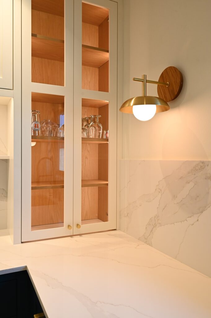 Butler's pantry with glass-front cabinets, wood interiors, marble backsplash, and brass sconce by RnD Builders Inc