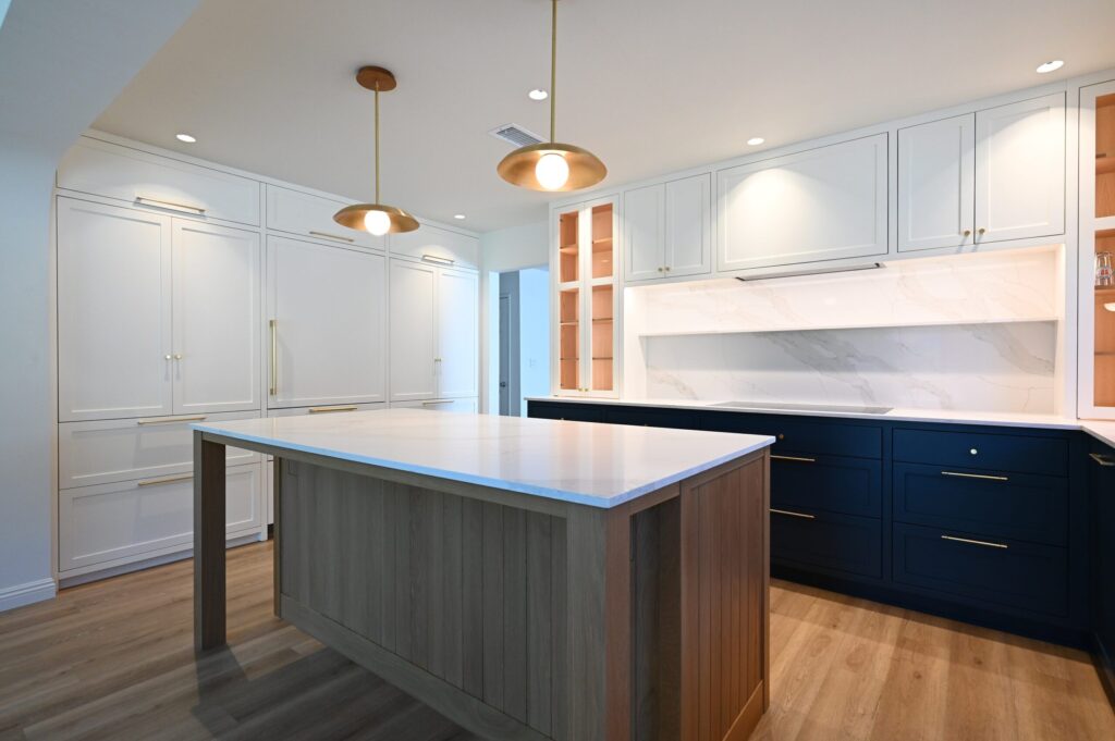 Transitional Kitchen with Navy Lower Cabinets Transitional kitchen with navy lower cabinets, gray wood island, white quartz countertops, and brass pendant lights by RnD Builders Inc