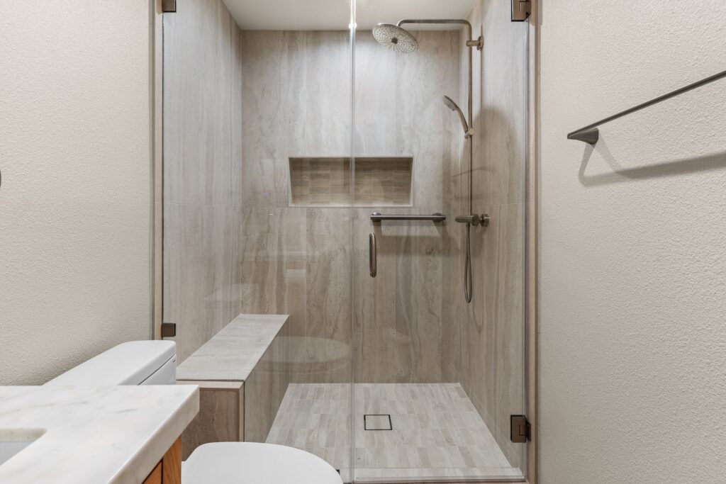 Walk-in glass shower with large-format stone-look tile, built-in niche, and brushed nickel fixtures in Thousand Oaks by RnD Builders Inc