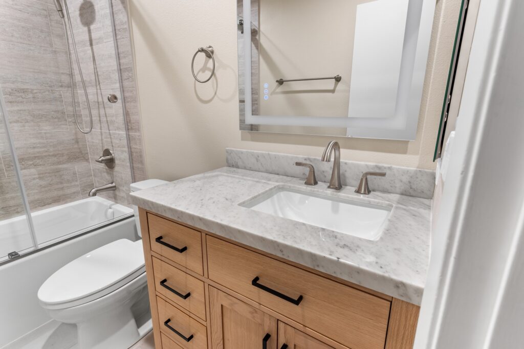 Full bathroom remodel with wood vanity, marble countertop, and tiled tub-shower combo in Thousand Oaks by RnD Builders Inc