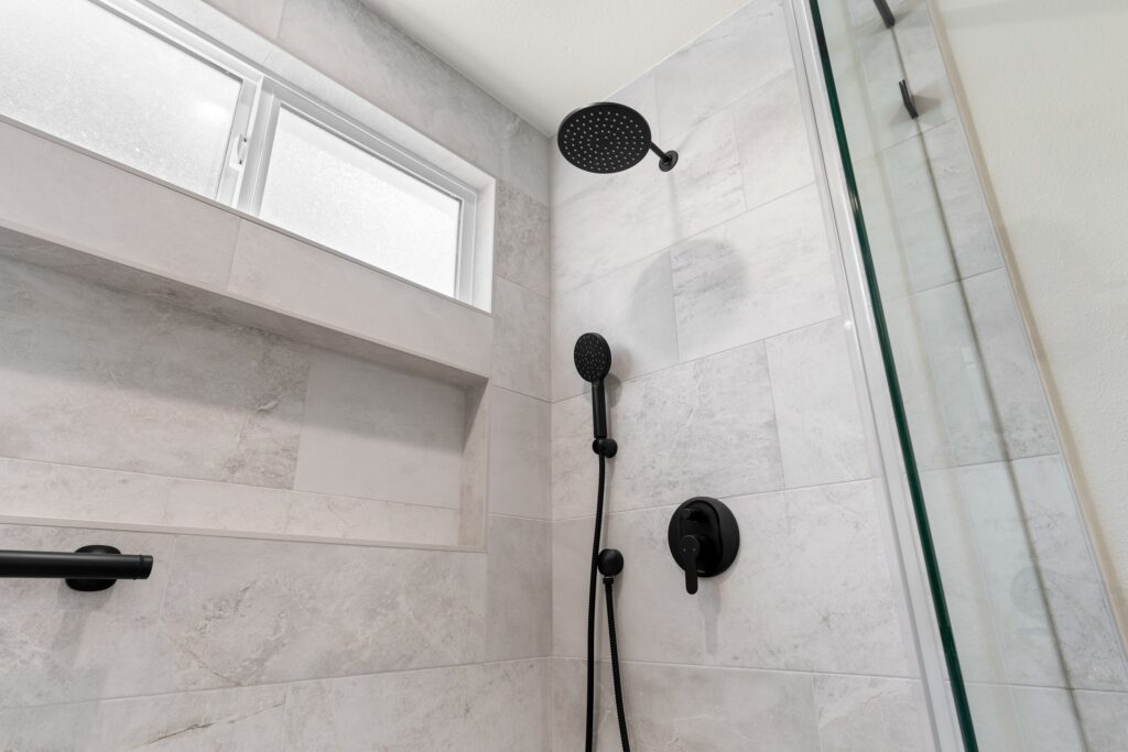 Walk-in shower with grey marble-look tile, black rain showerhead, and frameless glass door in Thousand Oaks by RnD Builders Inc