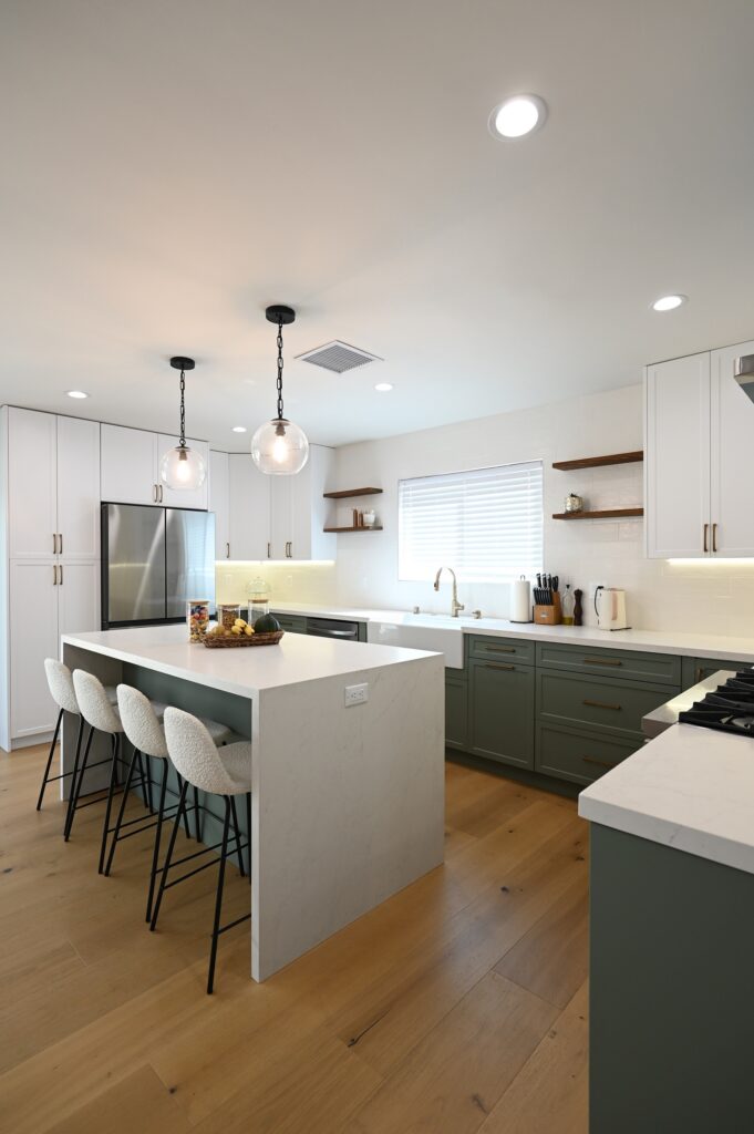 Modern kitchen with sage green lower cabinets, white uppers, quartz island, and globe pendants by RnD Builders Inc